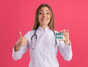 אישה מחייכת עם חלוק לבן מחזיקה תרופות ביד אחת וביד השניה מסמנת לייק